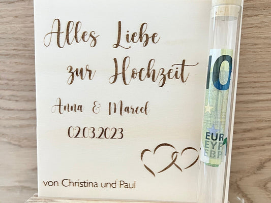 Geldgeschenk zur Hochzeit im Reagenzglas. Gravierte Holzplatte mit Alles Liebe zur Hochzeit. Namen des Brautpaares und das Hochzeitsdatum. Mit einer Halterung für das Reagenzglas, wo man das Geld einfügen kann.