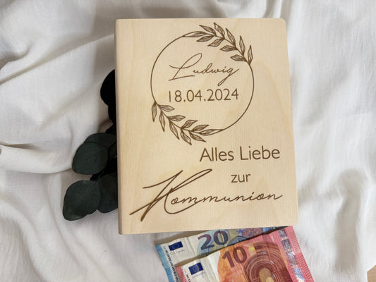 Geschenkidee zur Kommunion. Spardose aus Holz in Buchform graviert mit Namen und Datum des Kommunionskindes mit Blumenriing design.